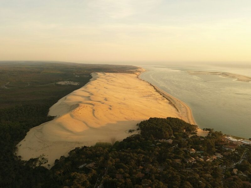 Vue aérienne de la dune du Pilat, de la forêt et du Bassin d’Arcachon dans une lumière dorée.