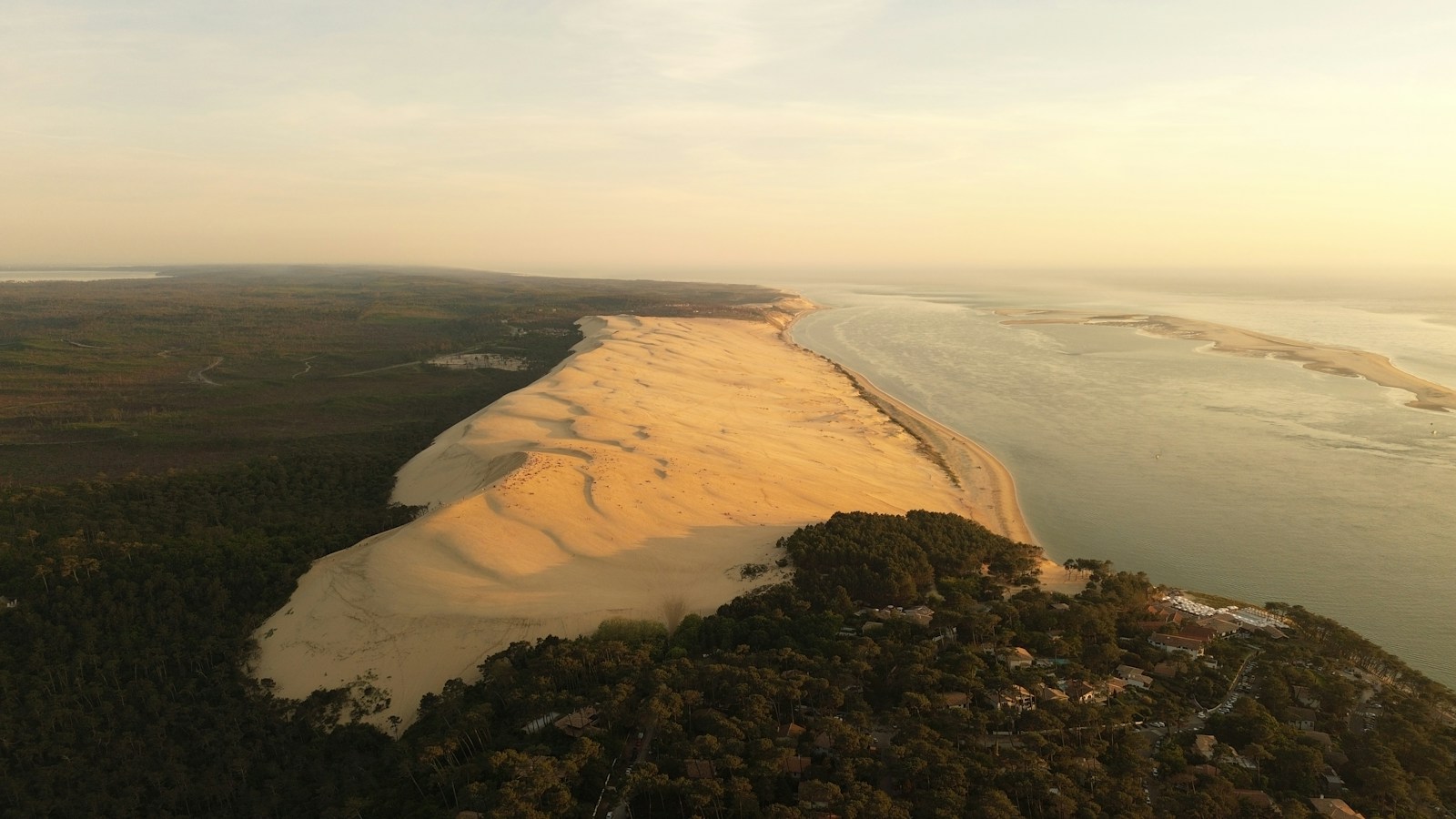 Vue aérienne de la dune du Pilat, de la forêt et du Bassin d’Arcachon dans une lumière dorée.